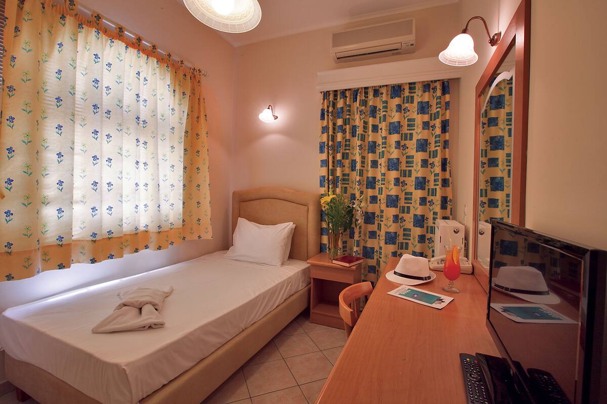 A hotel room with a single bed, a desk with a computer, a telephone, and a mirror.