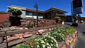 A hotel with a wooden deck, flower beds, and a sign indicating a trail ridge inn. - Alpine Trail Ridge Inn (Estes Park)