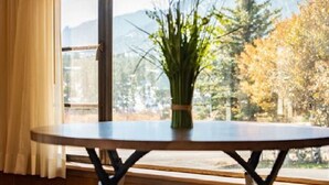 A room with a round table and three stools, a window with a view of trees and mountains, and a plant on the table. - Alpine Trail Ridge Inn (Estes Park)