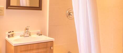 A bathroom with a wooden cabinet, a sink, a mirror, and a shower with a curtain.