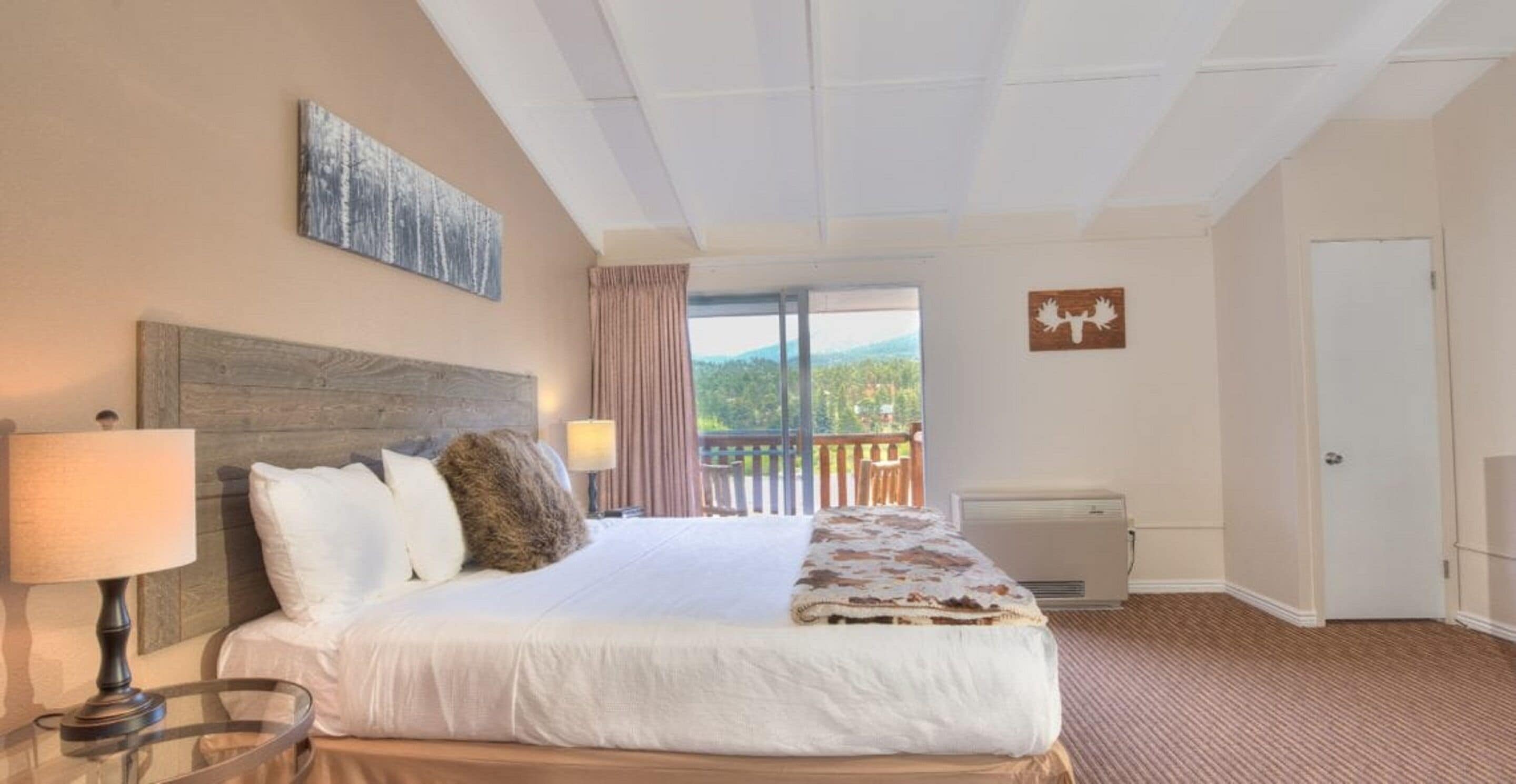 A hotel room with a large bed, a view of the outdoors, a balcony, and a mounted artwork.