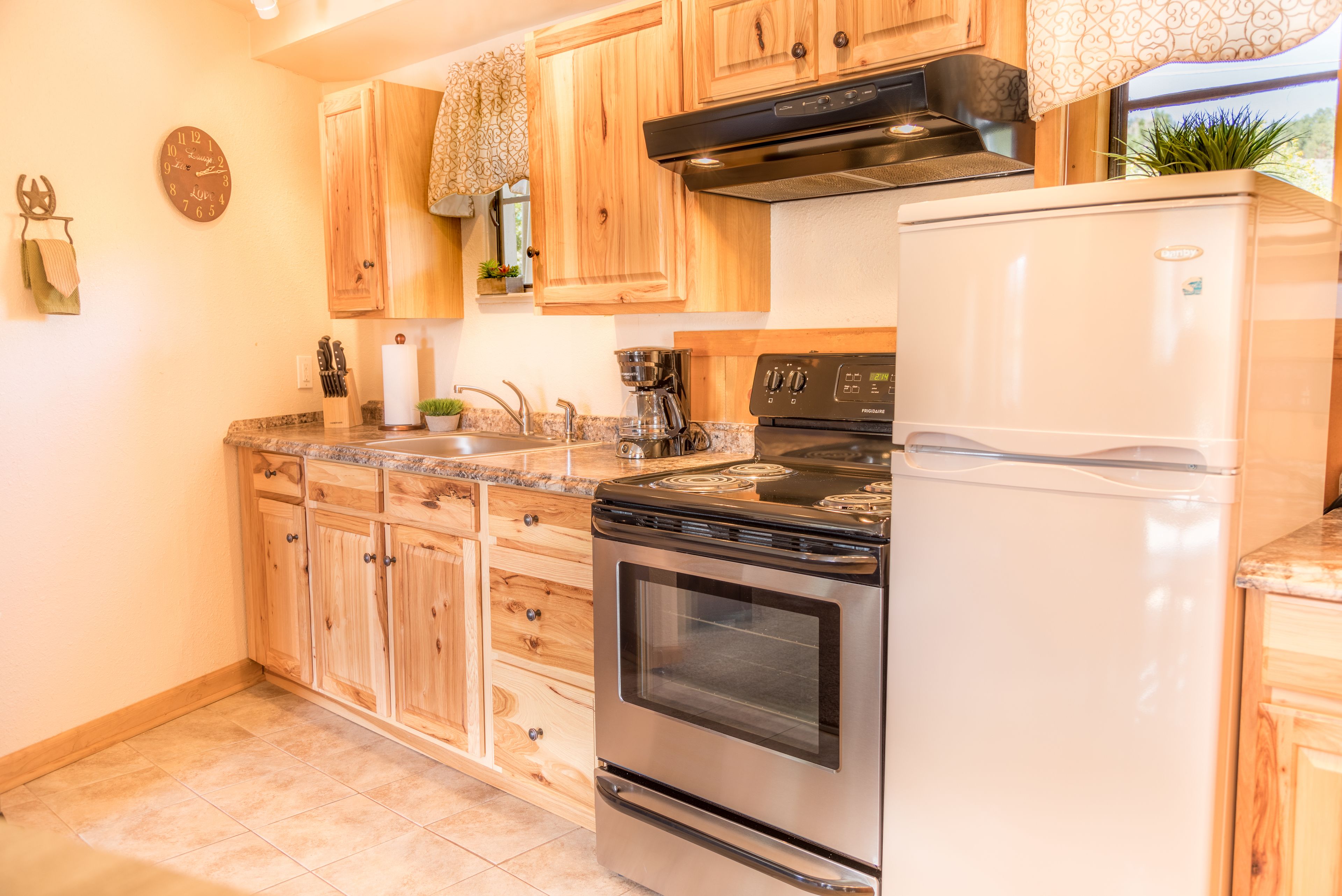 Una cocina con armarios de madera, estufa de acero inoxidable, refrigerador blanco y un reloj en la pared.