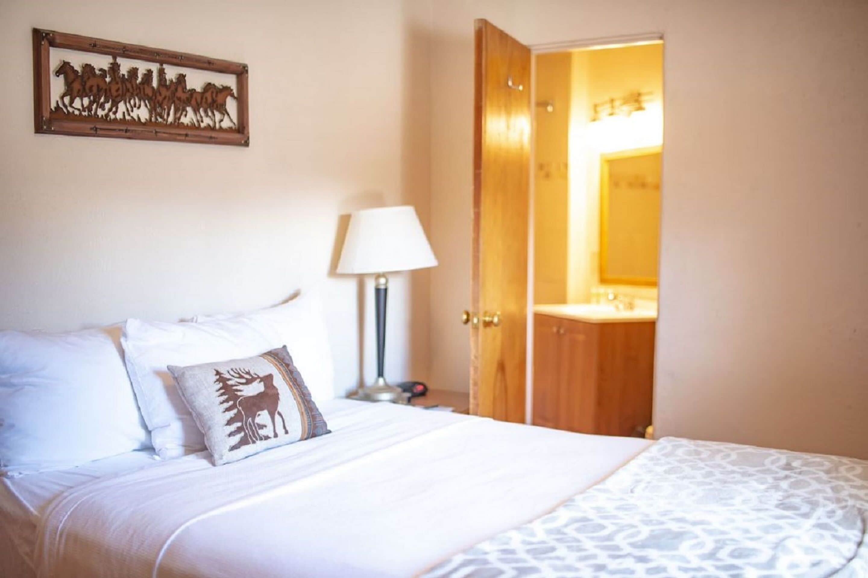 Un dormitorio con una cama, una mesita de noche, una lámpara y una puerta de madera que da a un baño.