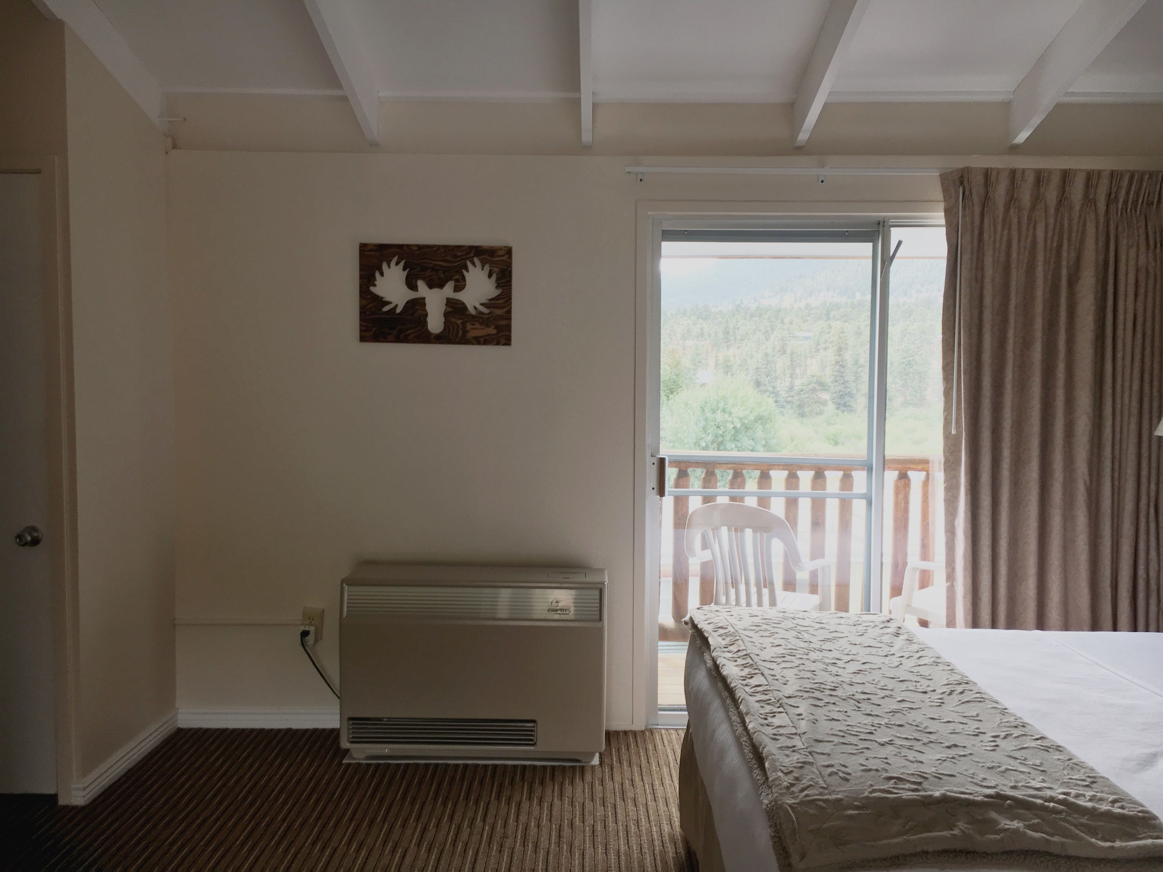 Un dormitorio con cama, un radiador, una ventana con cortinas y vistas a la vegetación exterior.