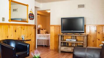 Una habitación con pared de paneles de madera, un televisor sobre un mueble de madera, una cama con colcha blanca y un sillón de cuero negro.
