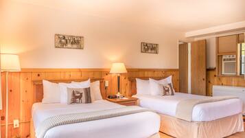 A hotel room with two beds, wooden headboard, wall-mounted lamps, and a window with blinds.