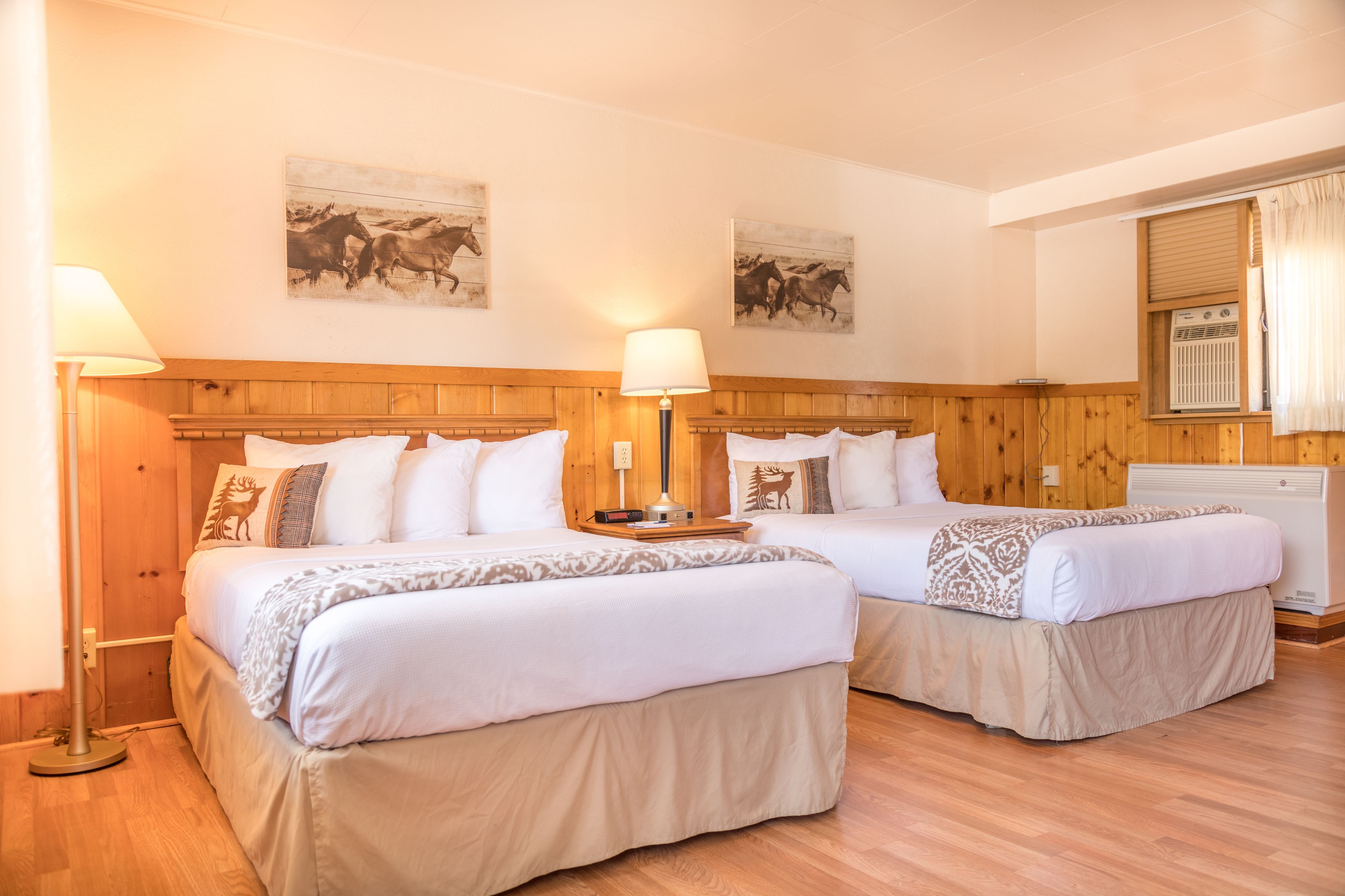 Une chambre d’hôtel avec deux lits, des têtes de lit en bois, du linge de lit blanc et deux lampes fixées au mur.