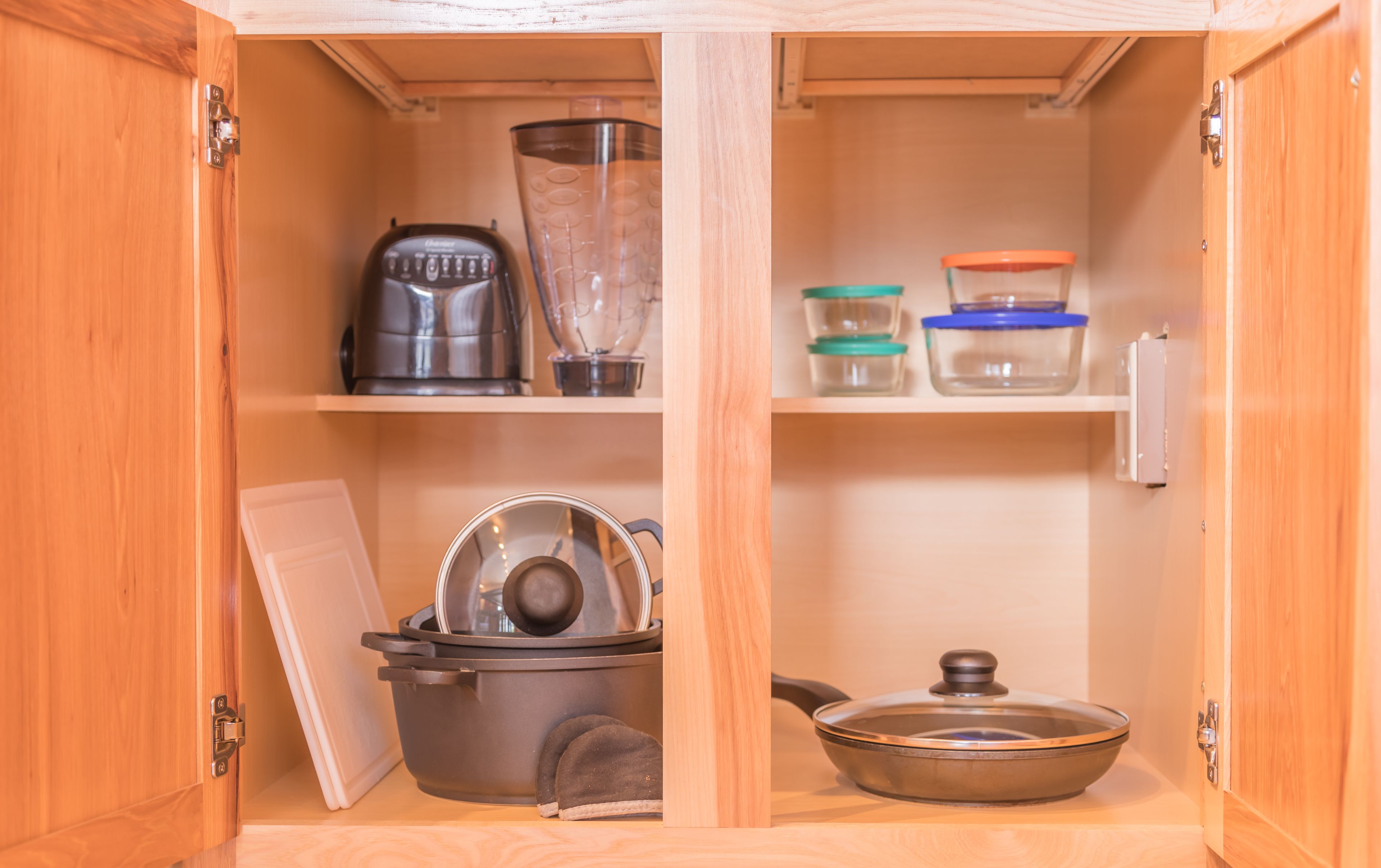 A kitchen cabinet with a kettle, blender, pots, and storage containers.