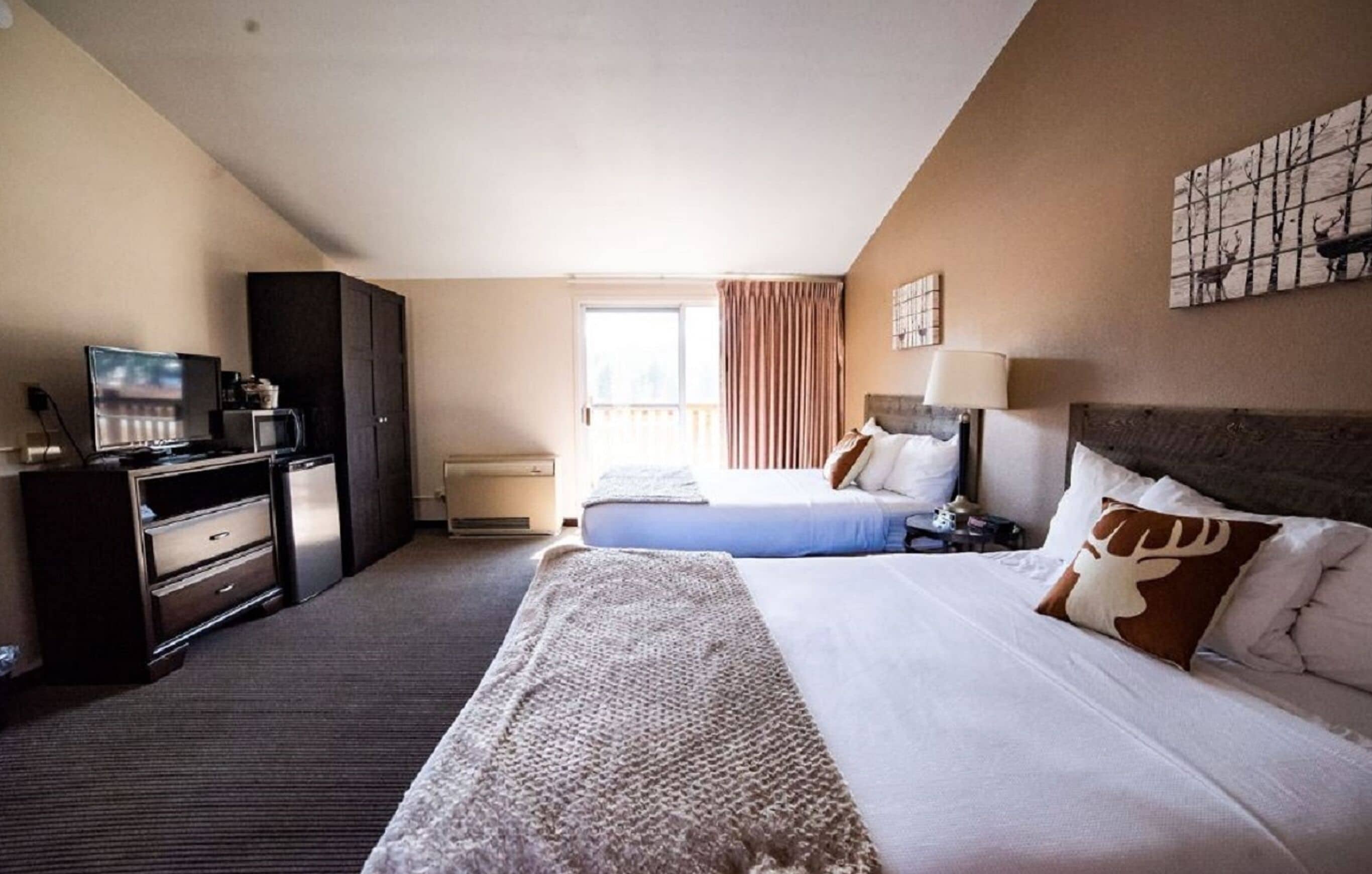 A hotel room with a bed, a desk with a computer, a television, and a window with curtains.