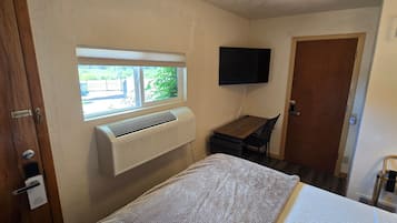 Una habitación pequeña con cama, escritorio, silla, ventana y televisor montado.