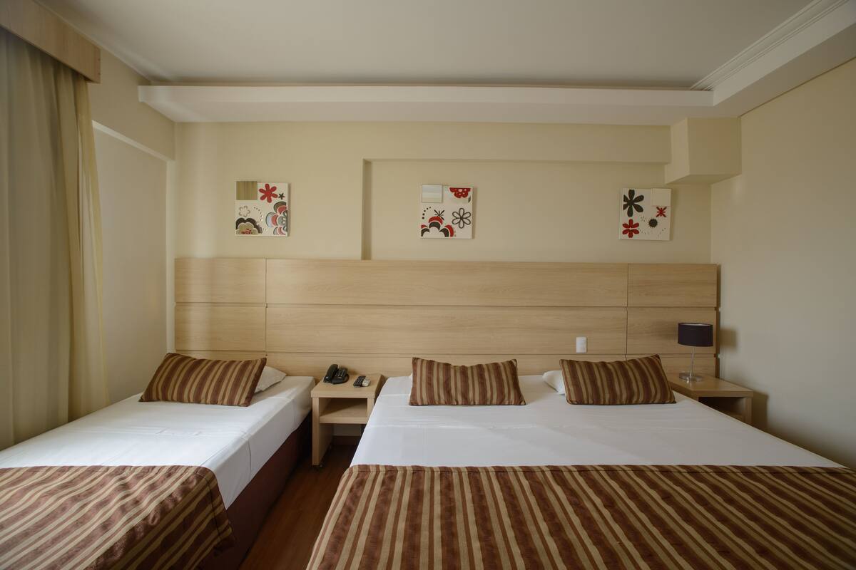 A hotel room with two single beds, a wooden headboard, bedside tables with lamps, and wall art.