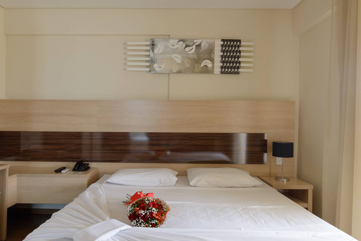 A hotel room with a wooden headboard, a bedside table with a lamp, a phone, and a bouquet of flowers on the bed.