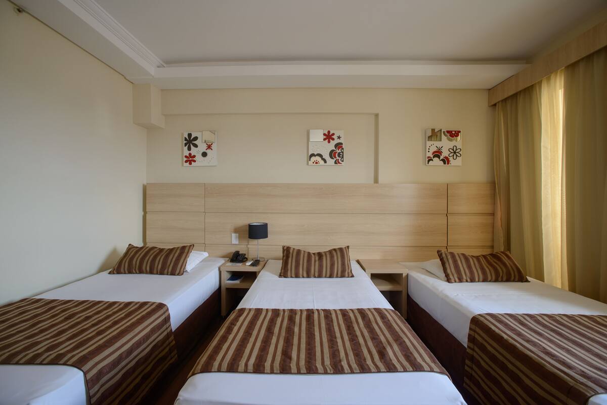 A hotel room with three single beds, a wooden headboard, and three wall-mounted artworks.