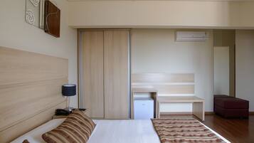 A hotel room with a bed, bedside table, lamp, wardrobe, and a small desk with a chair.