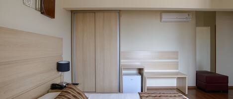 A hotel room with a bed, bedside table, lamp, wardrobe, and a small desk with a chair.