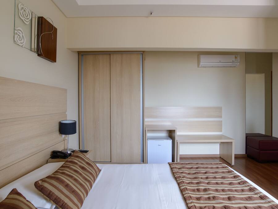 A hotel room with a bed, bedside table, lamp, wardrobe, and a small desk with a chair.