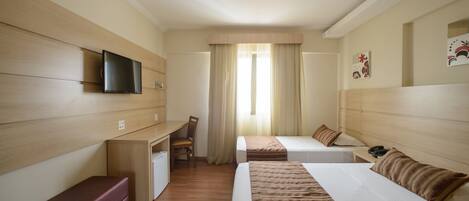 Habitación de hotel con cama, escritorio, silla, televisión y ventana con cortinas.