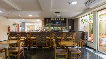 A restaurant with a bar area, multiple wooden tables and chairs, and a view of the outside through large windows.