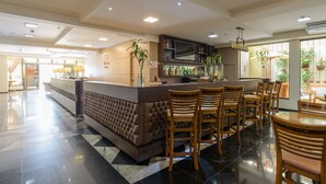 A bar area with a bar counter, multiple wooden bar stools, a television, and potted plants. - Faro Hotel (Atibaia)