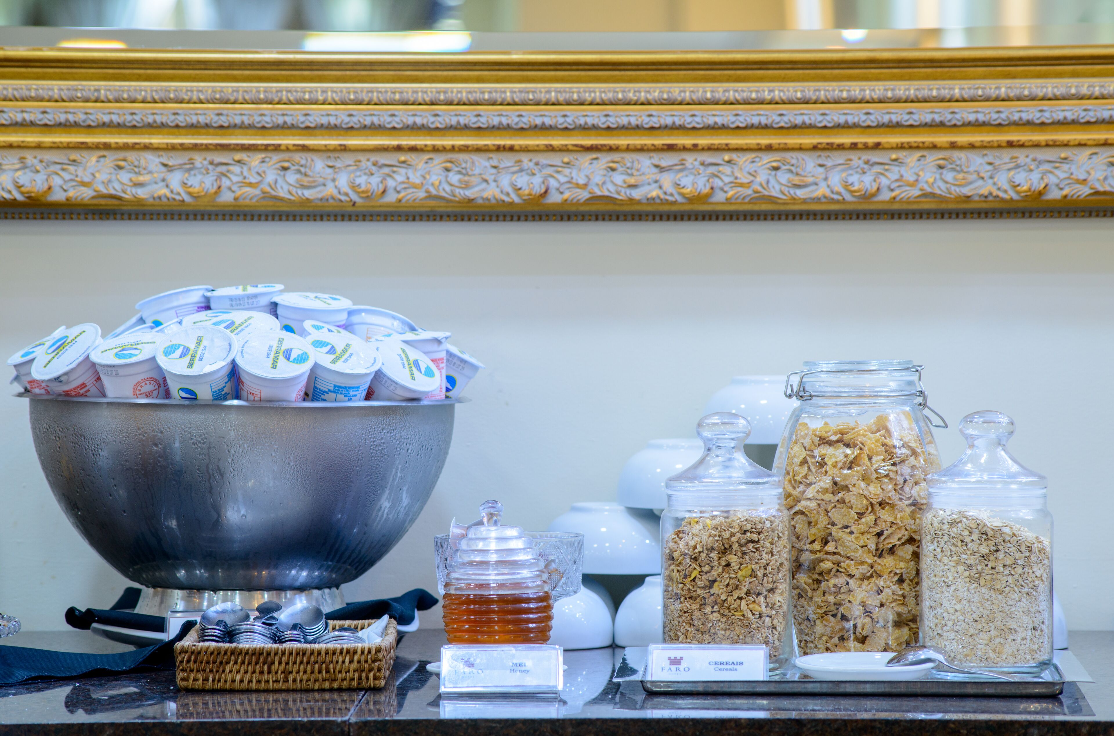Un buffet avec un grand saladier en métal rempli de pots de yaourt, deux bocaux en verre de granola et un petit bocal en verre de miel.