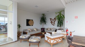 A modern living room with a sofa set, two side tables, a coffee table, and a dining table. There are two potted plants and a fire extinguisher on the wall. - Faro Hotel (Atibaia)