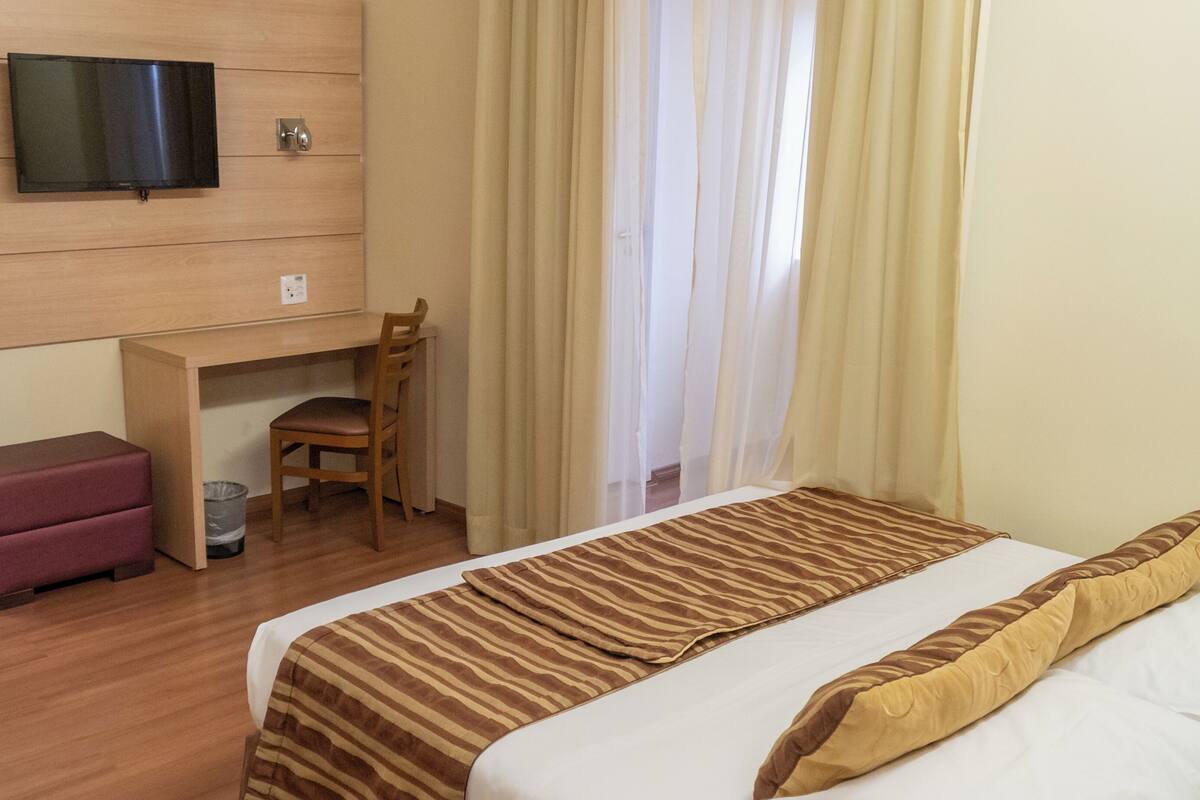 A hotel room with a bed, a desk, a chair, and a television on the wall.