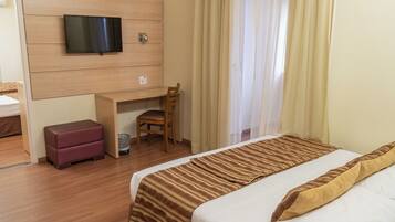 Een hotelkamer met een bed, een bureau, een stoel en een televisie aan de muur.
