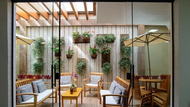 A cozy indoor seating area with wooden furniture, potted plants, and a glass partition. - Faro Hotel (Atibaia)
