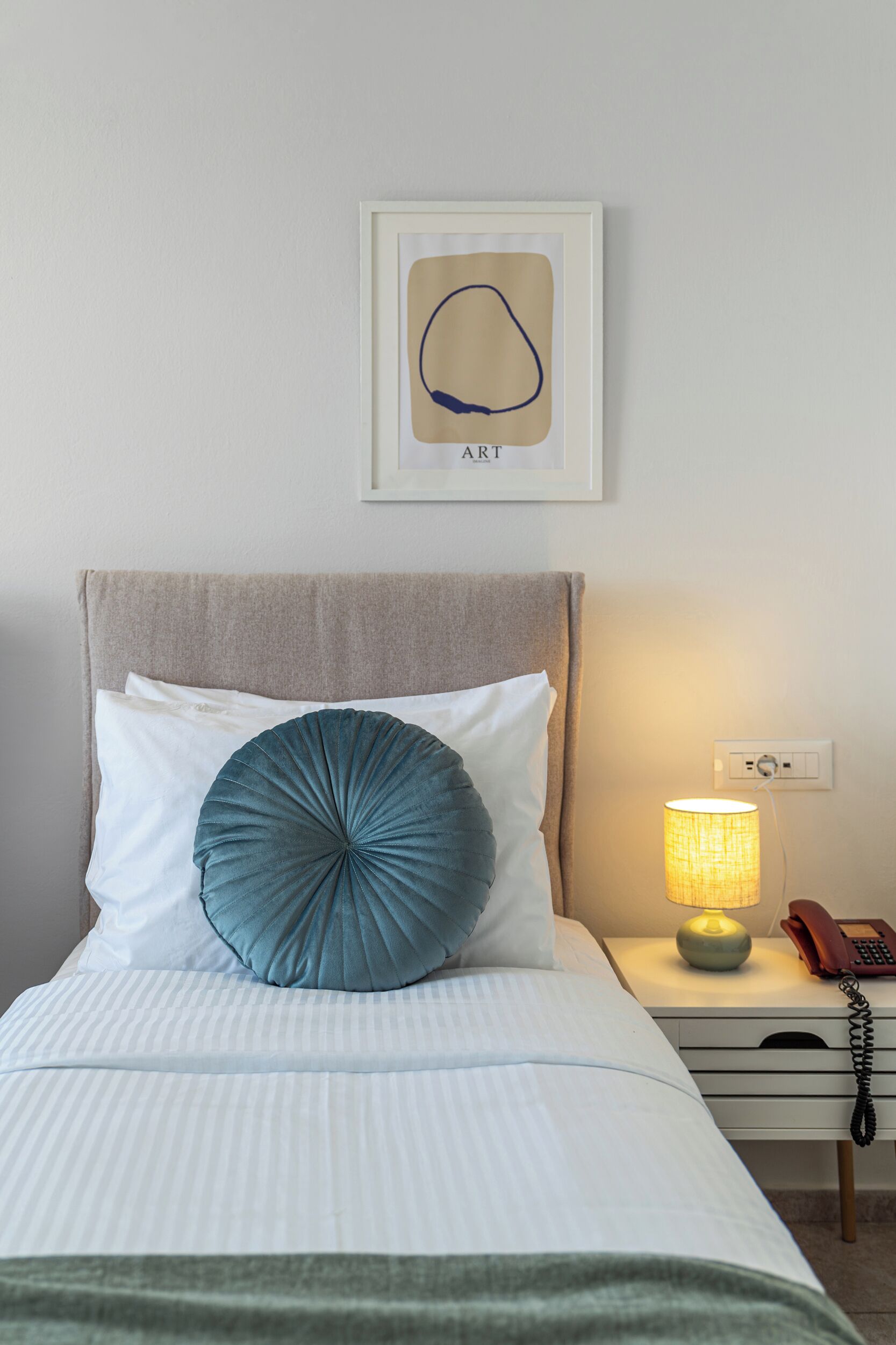 A neatly made bed with a pillow, a bedside lamp, and a framed picture on the wall.