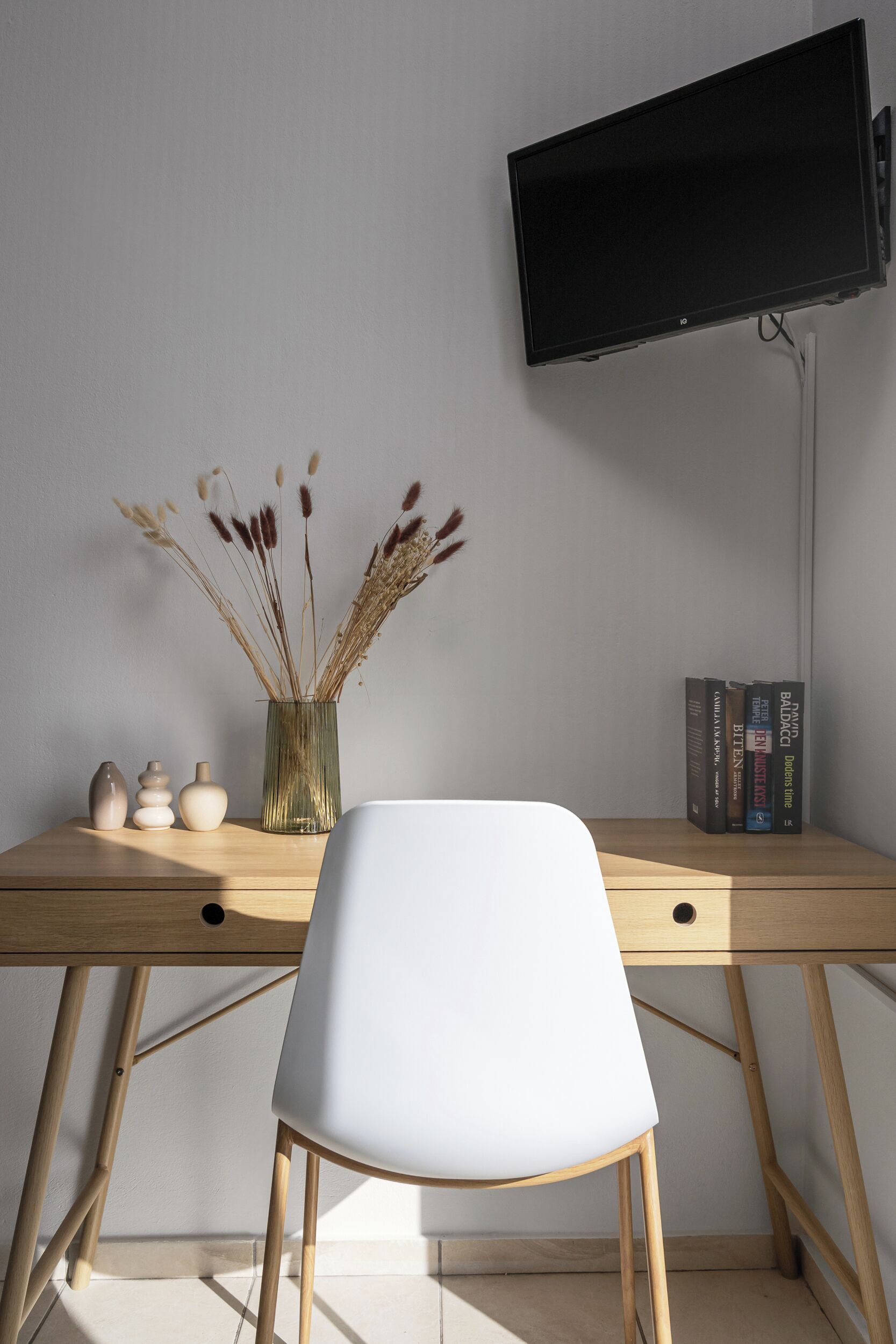 A desk with a white chair, a vase with dried plants, and books.