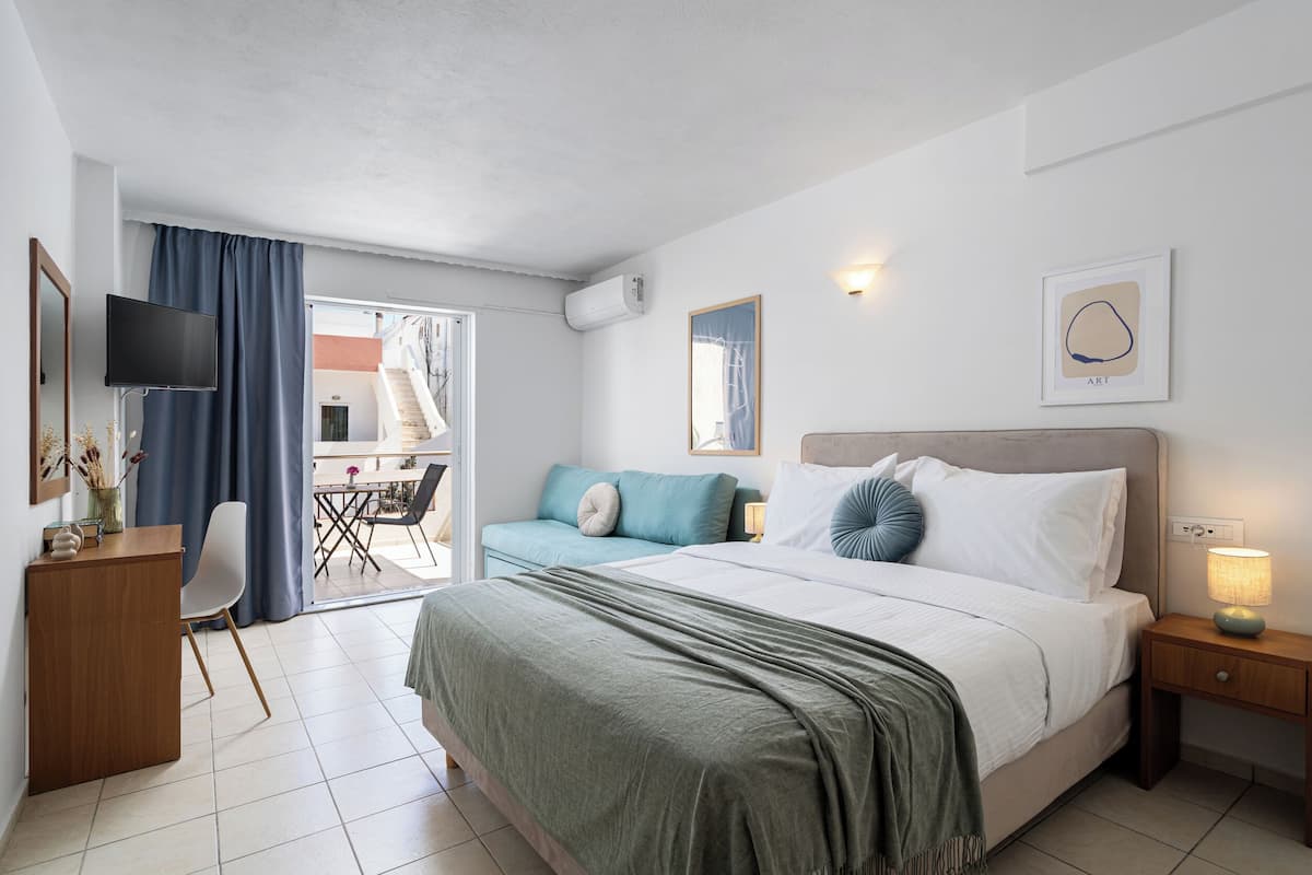Una habitación de hotel con cama, escritorio, televisor, sofá y balcón.