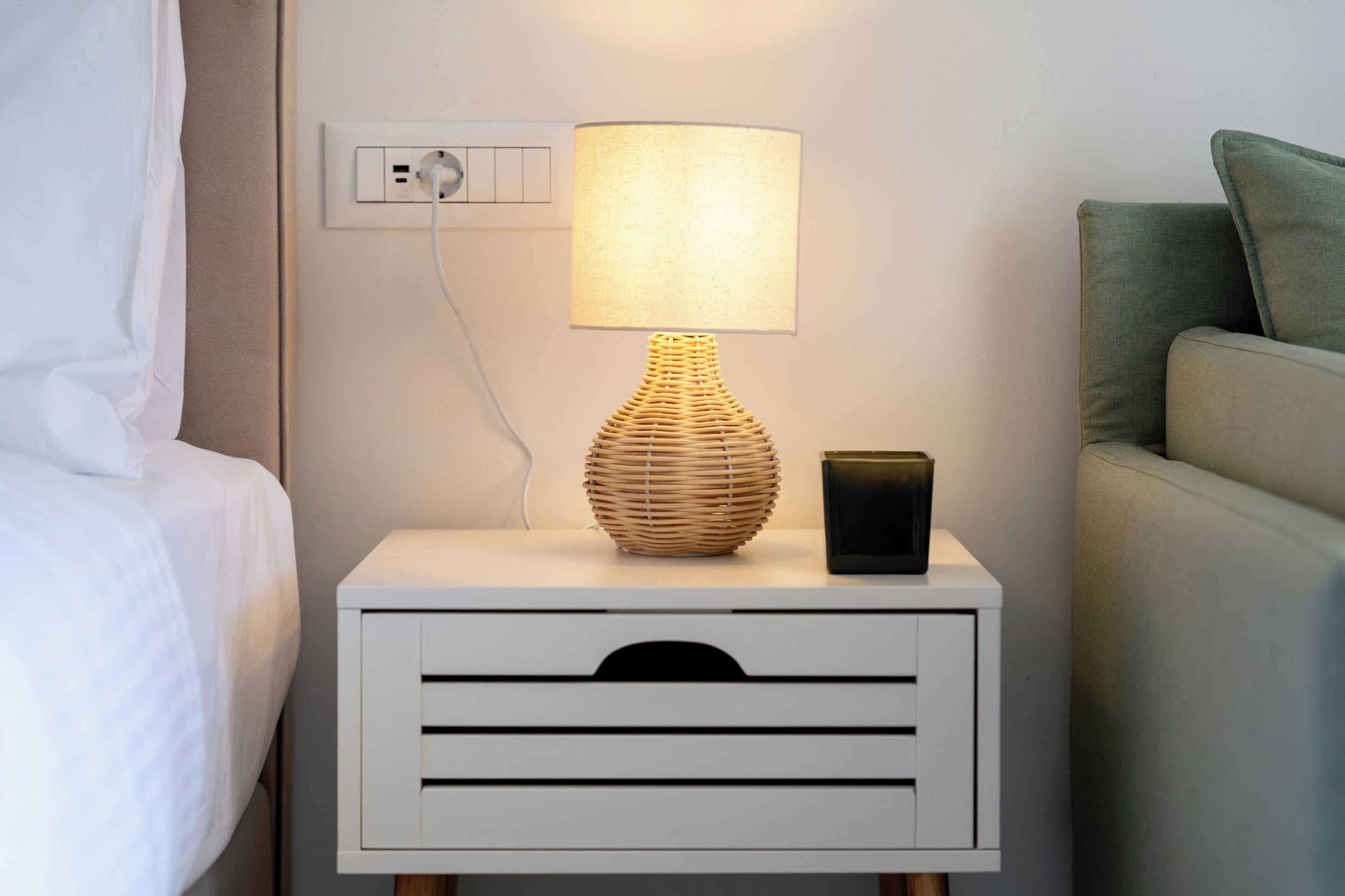 A bedside table with a lamp, a power outlet, and a nightstand drawer.
