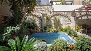 A swimming pool surrounded by lush greenery and stone architecture. - Hotel Flisvos (Sitia)