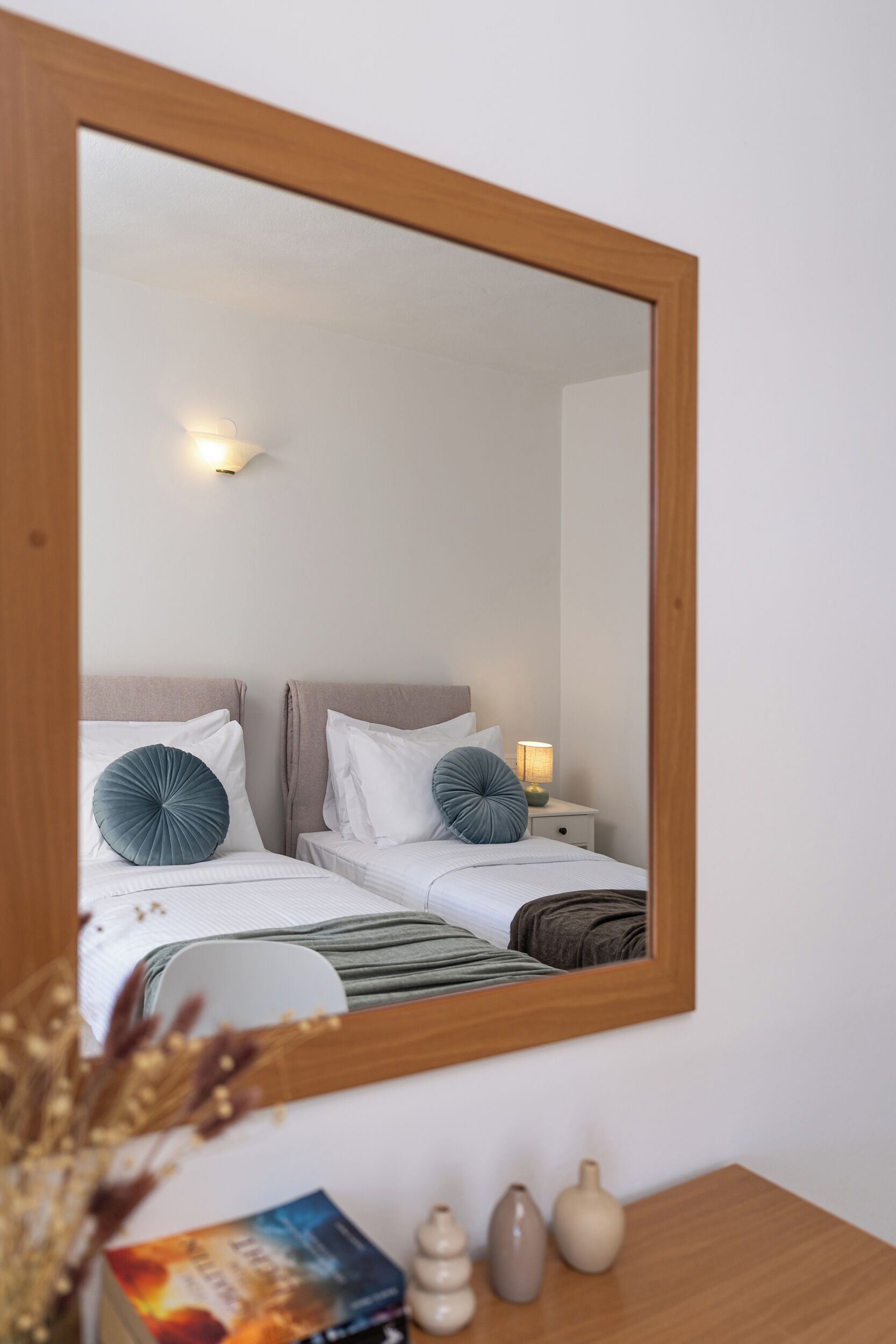 Quarto de hotel com duas camas, uma mesa de cabeceira com abajur e um espelho na parede.