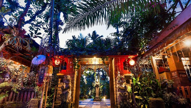 Una entrada ornamentada con un pilar central, rodeada de exuberante follaje tropical y detalles decorativos.
