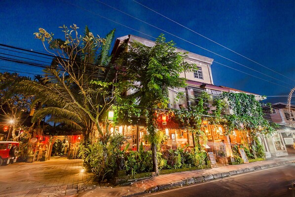 A building with a restaurant on the ground floor, surrounded by greenery and illuminated by warm lights.