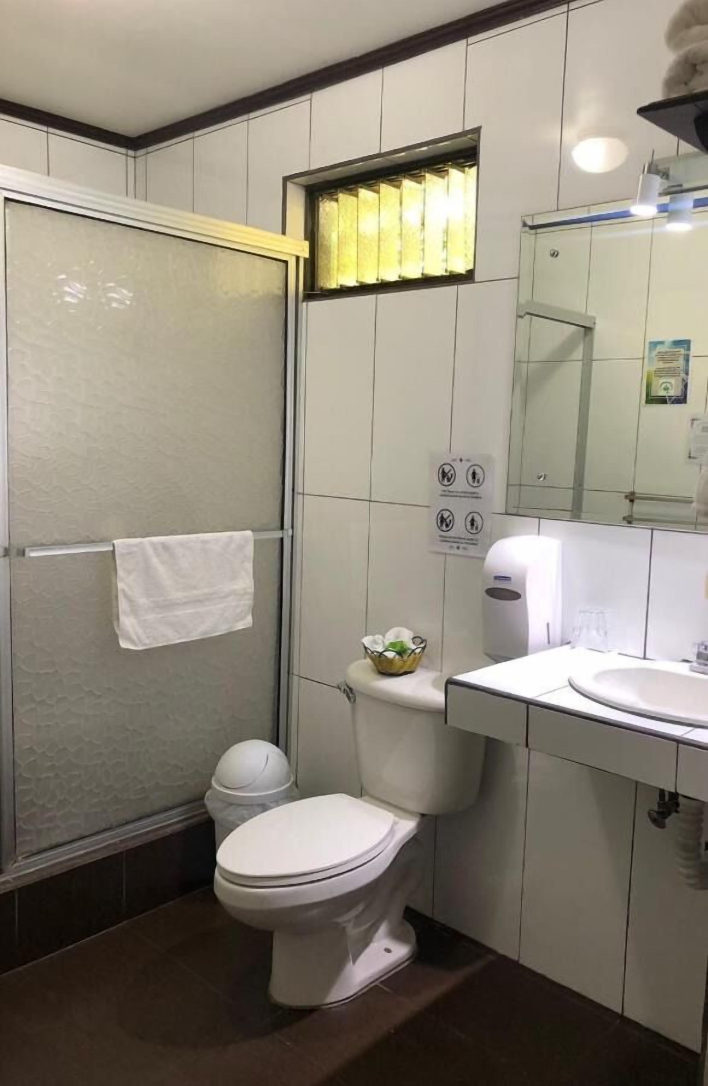 Un baño con inodoro, lavamanos, espejo y zona de ducha.