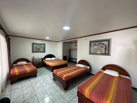 A hotel room with three single beds, a wooden nightstand, a small table, and two framed pictures on the walls.