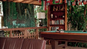 Une table de billard recouverte d’un drap vert, entourée d’une clôture en bois et d’une végétation luxuriante.
