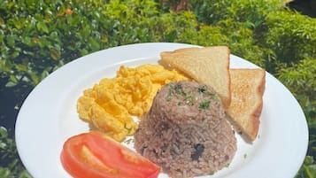 Un plato de comida con huevos revueltos, arroz, tostada y una rodaja de tomate.
