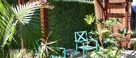 An outdoor seating area with a wooden pergola, green chairs, and a neatly trimmed hedge in the background.