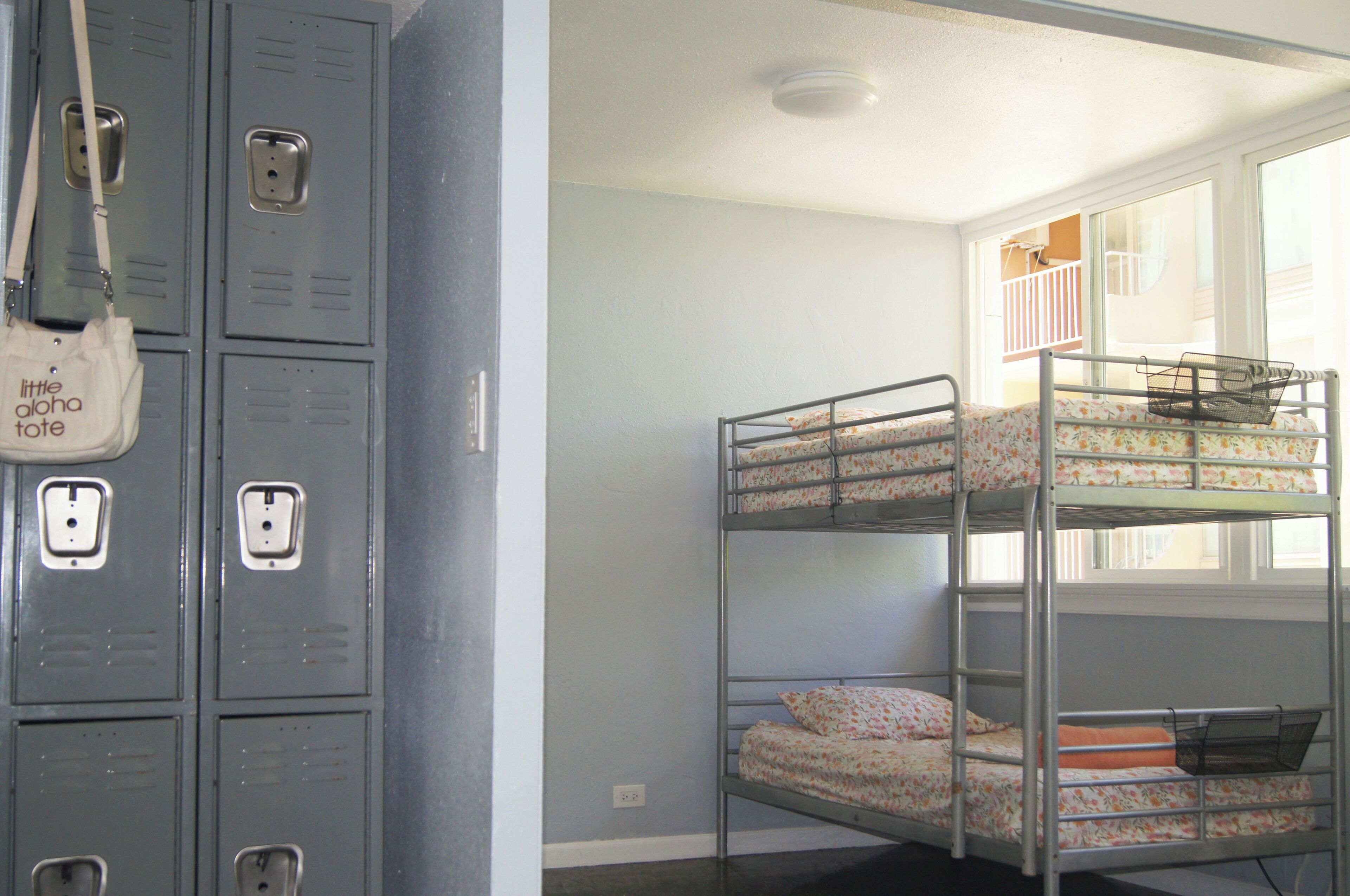 Bunk beds with floral bedding, a window with a view, and a row of lockers.