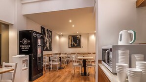 En restaurant med trægulv, hvide borde og stole, en automat og en mikroovn på disken.