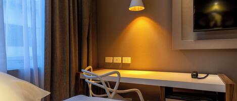 Habitación de hotel con cama, escritorio, silla, televisor y mesita de noche.