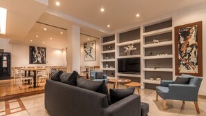 En moderne stue med sofa, lænestole og fjernsyn. Reoler med dekorative genstande og kunstværker.