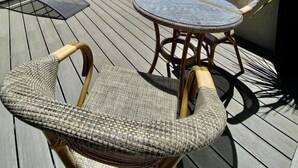 En tagterrasse med fletningsmøbler, et glasbord og plantetpotter.