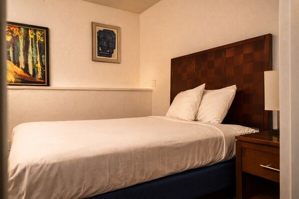 Una habitación de hotel con una cama, una mesita de noche, una lámpara y dos cuadros en la pared.