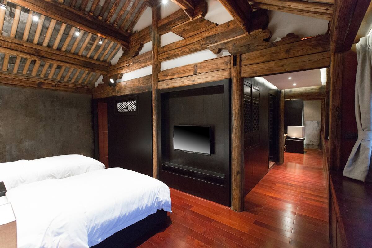 Ein Zimmer mit Holzbalken, einem Bett, einem Fernseher und einem Spiegel.