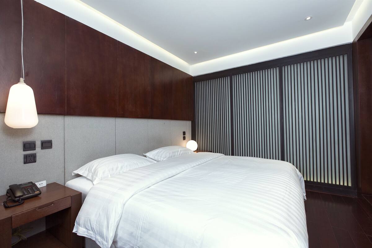 Ein modernes Hotelzimmer mit einem großen Bett, einem Nachttisch mit Telefon und einer Wandleuchte.