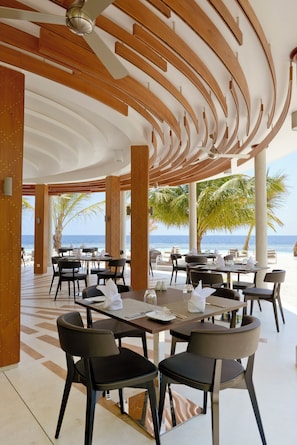 Un ristorante sulla spiaggia con tavoli e sedie, palme e vista sull'oceano.